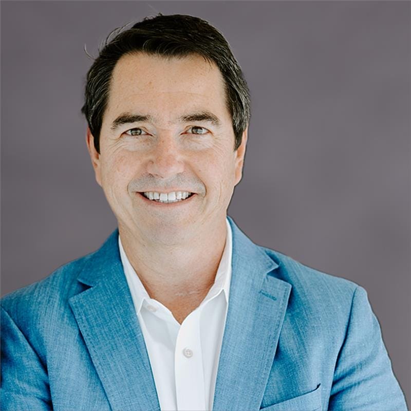 Man in a blue blazer smiling against a gray background.